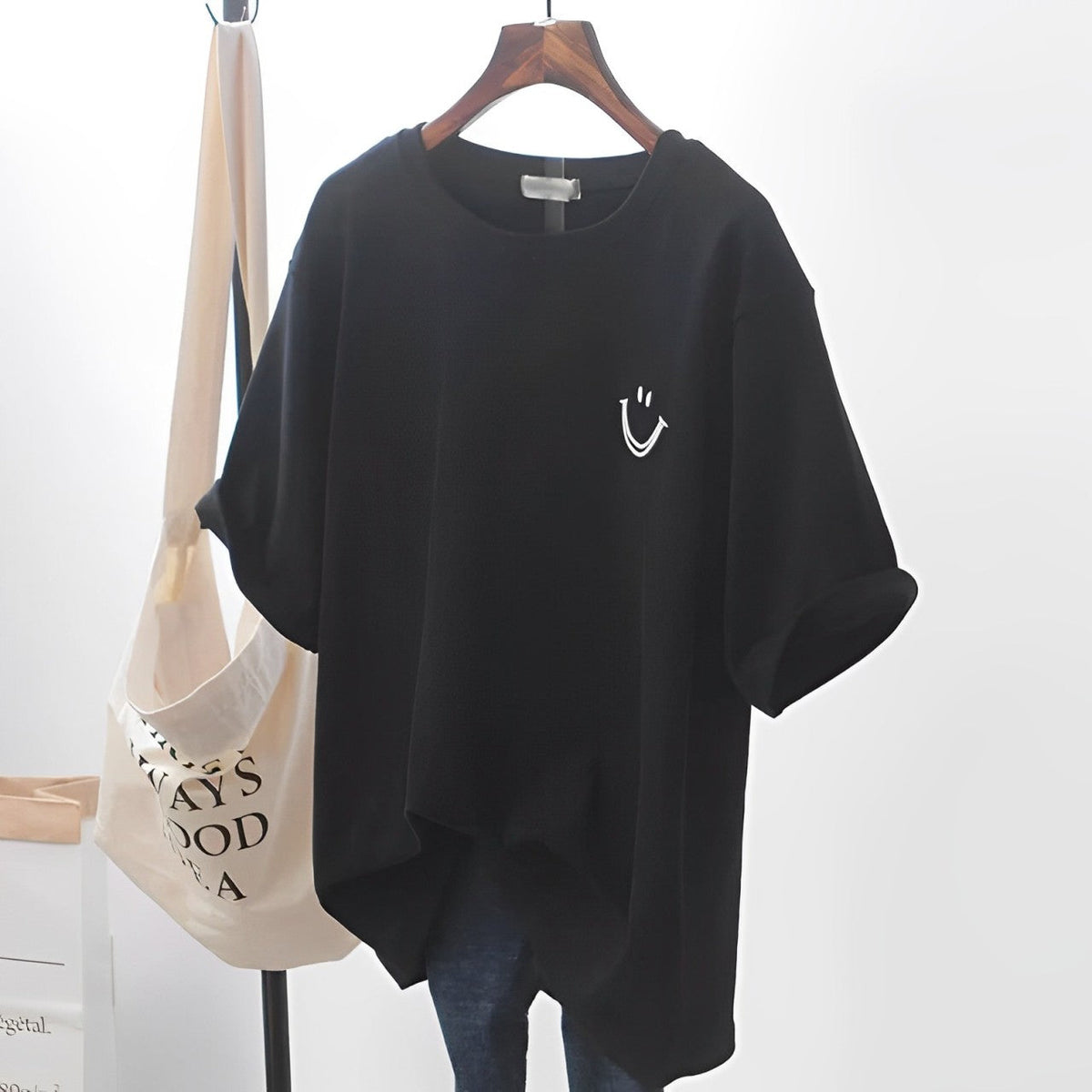 Black oversized T-shirt with an embroidered smile face, shown on a hanger