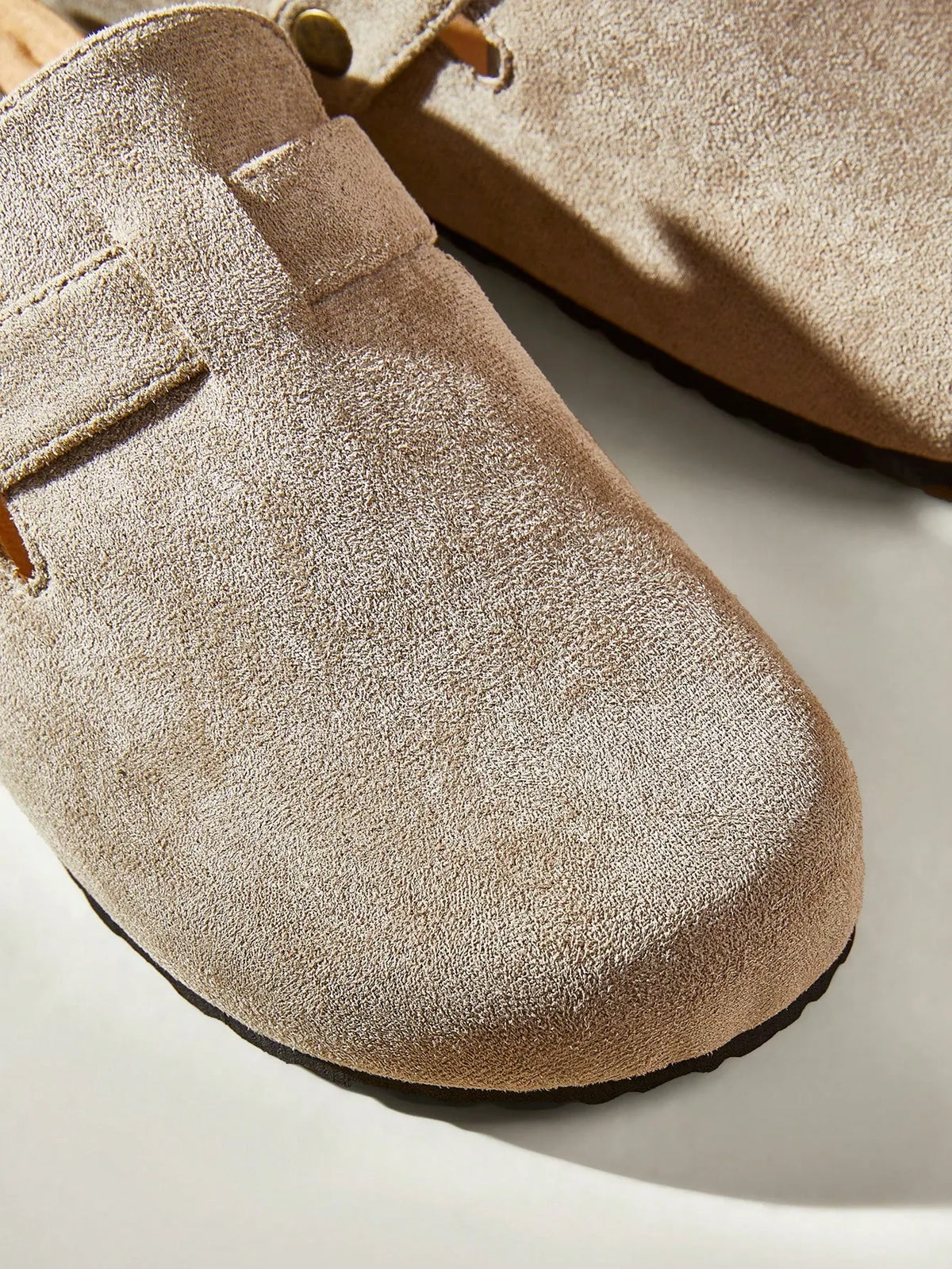 Close-up of the suede toe and buckle strap of a taupe clog-style slide