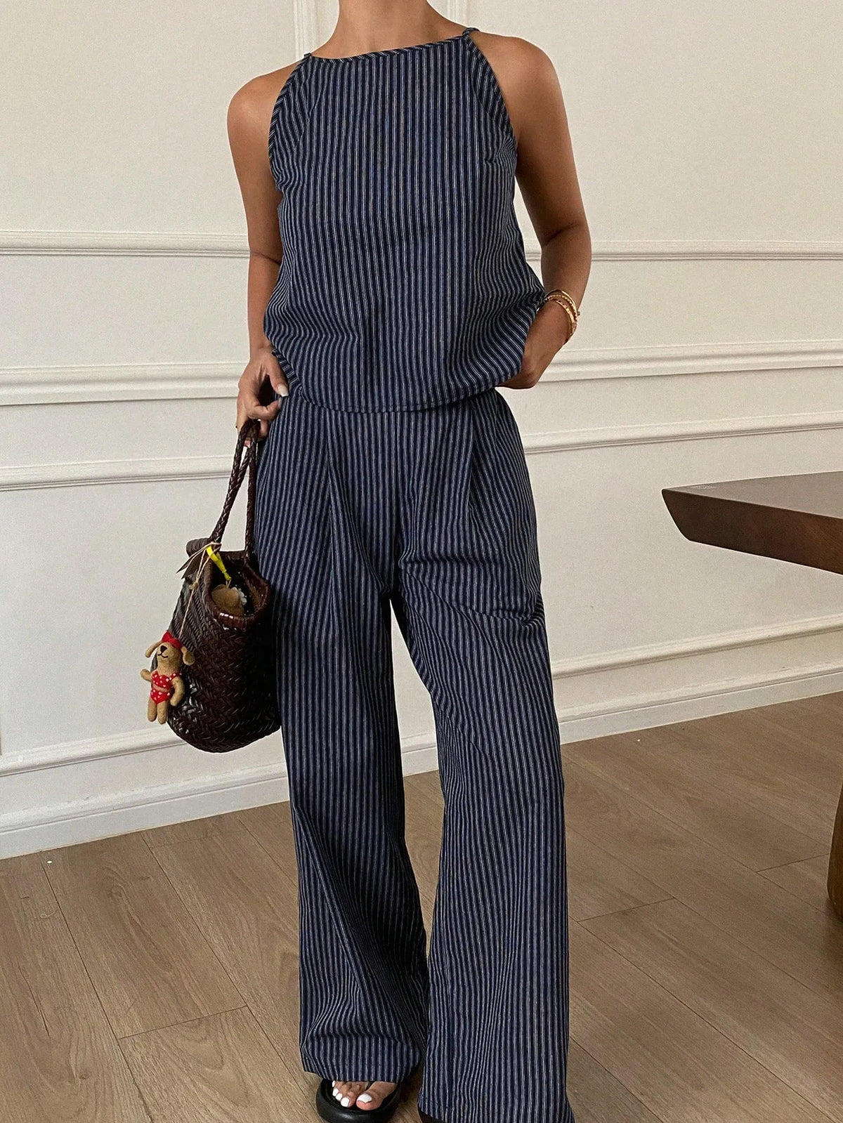 Close front view of the navy pinstripe halter-neck top and pleated wide-leg pants, one hand in the pocket