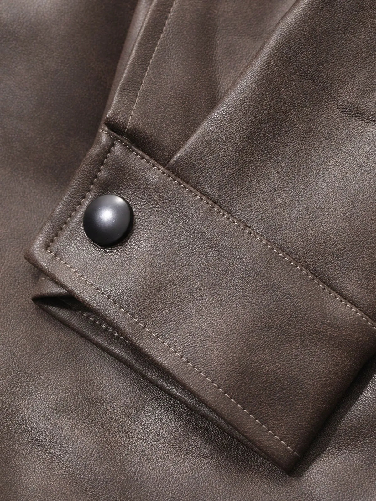 Close-up of the snap button on the pocket flap of the brown leather-look jacket