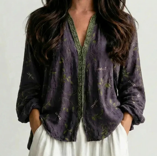 Woman wearing a dark purple floral boho V-neck blouse with green trim and white pants, front view