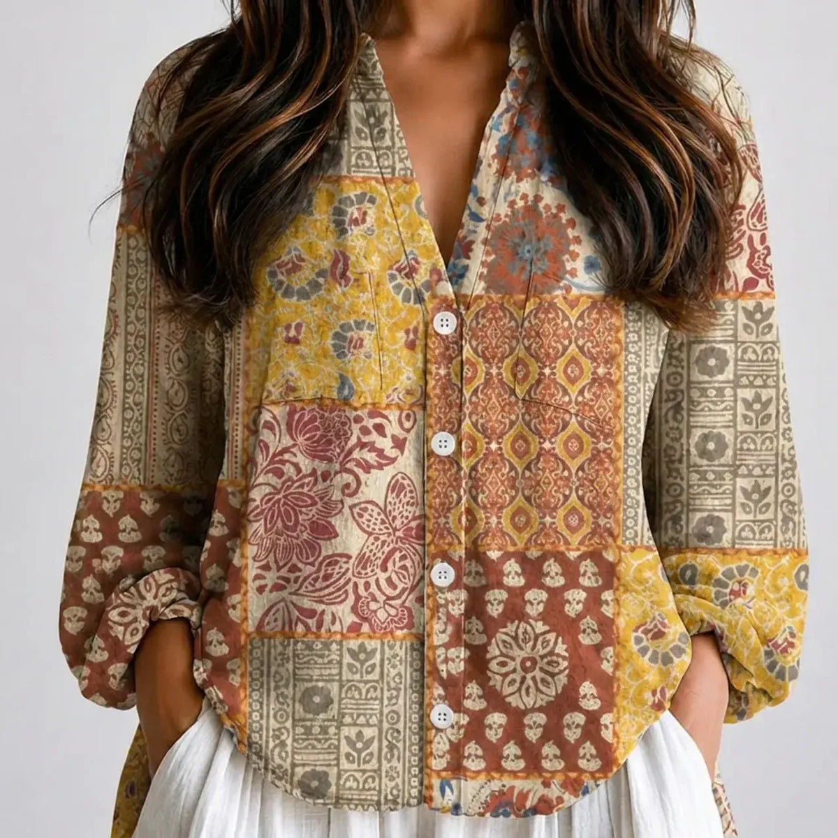 Woman wearing a patchwork print boho V-neck blouse in mustard, rust and cream with white pants