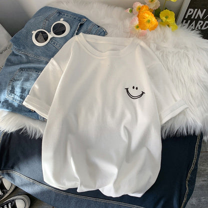 White casual T-shirt with an embroidered smile face, laid flat on denim