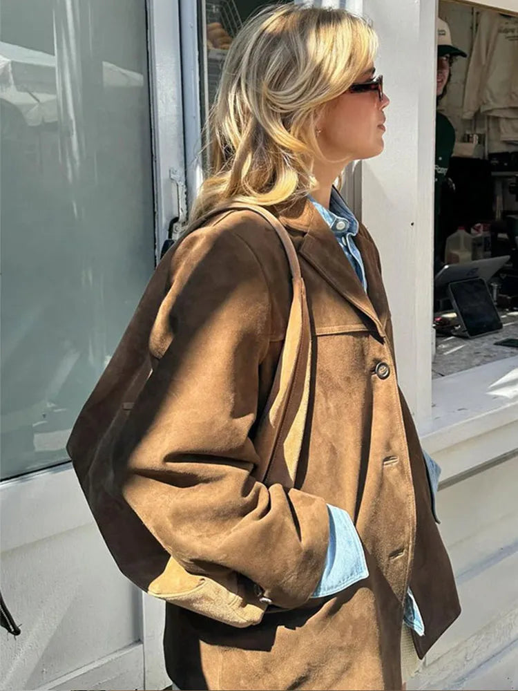 Woman wearing the brown suede-look jacket over a light blue shirt, side view outdoors