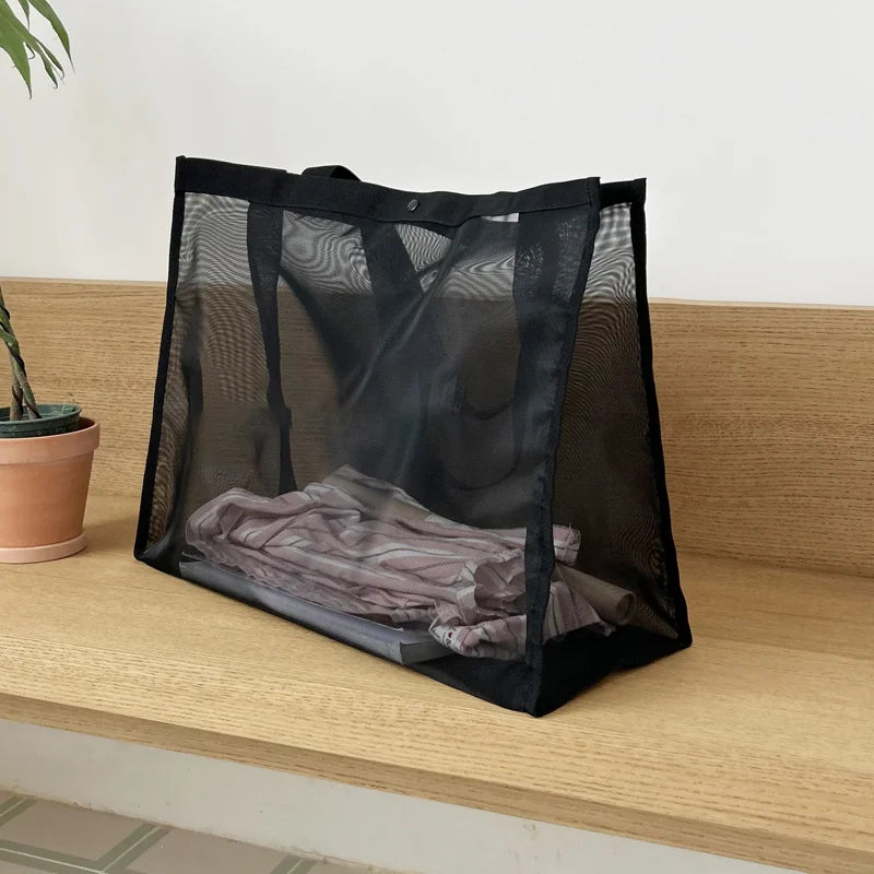 Black sheer mesh bag with folded clothes visible inside, on a wooden shelf