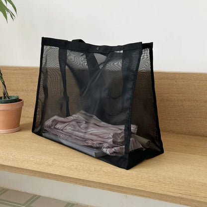 Black sheer mesh bag with folded clothes visible inside, on a wooden shelf