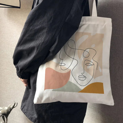 Canvas bag with a two-face line-art print in muted pastel shapes, carried on the shoulder