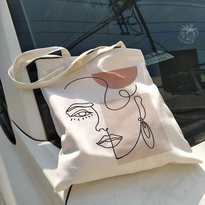 Natural canvas bag with a line-art face print, placed on a car hood