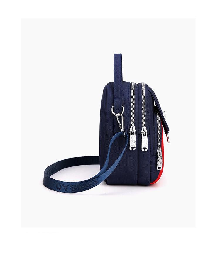 Side view of the navy shoulder bag showing its zip compartments