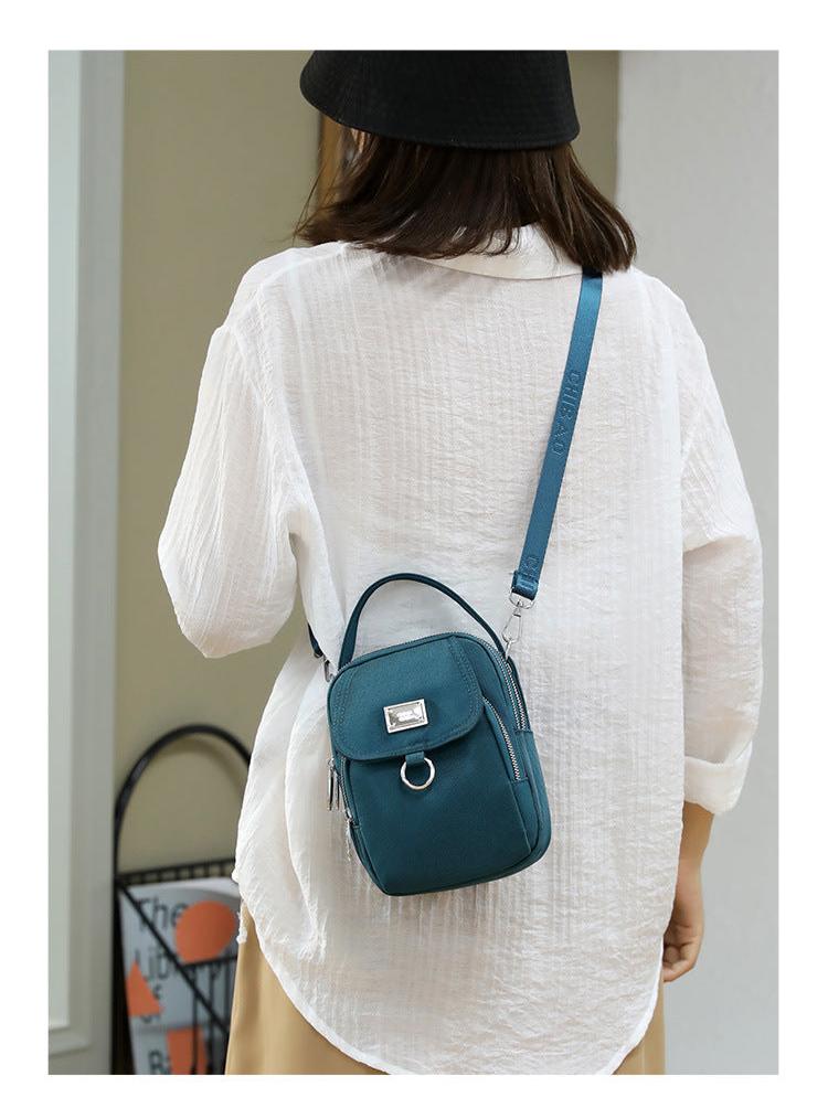 Small teal shoulder bag worn crossbody over a white shirt, back view