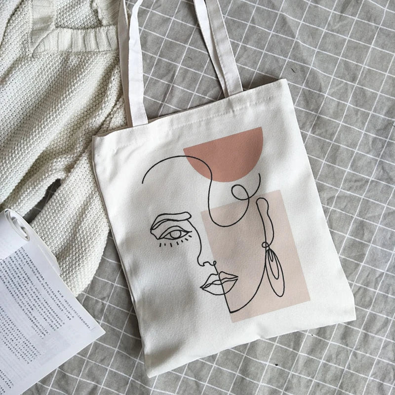 White canvas bag with an abstract line-art face print in black and blush pink