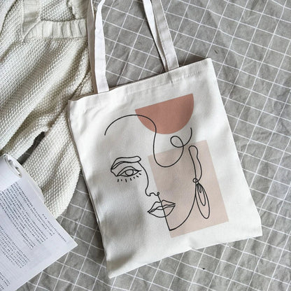 White canvas bag with an abstract line-art face print in black and blush pink