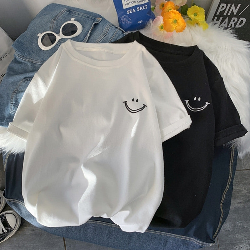 White and black smile face T-shirts laid flat on a denim jacket with sunglasses and flowers