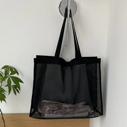 Black sheer mesh bag hanging from a wall hook with folded clothes inside