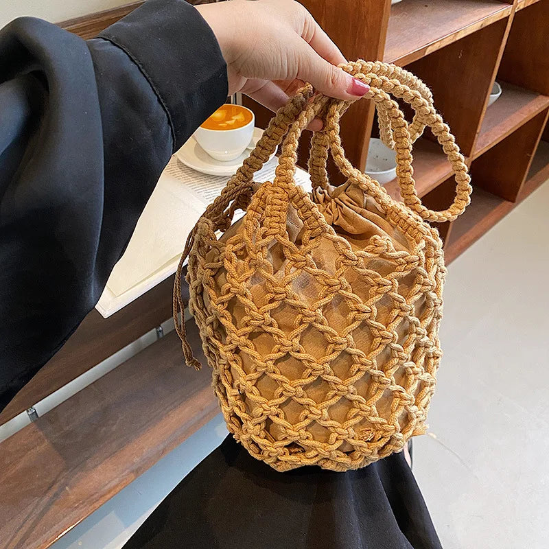 Hand holding the tan knotted-rope bucket bag by its handles