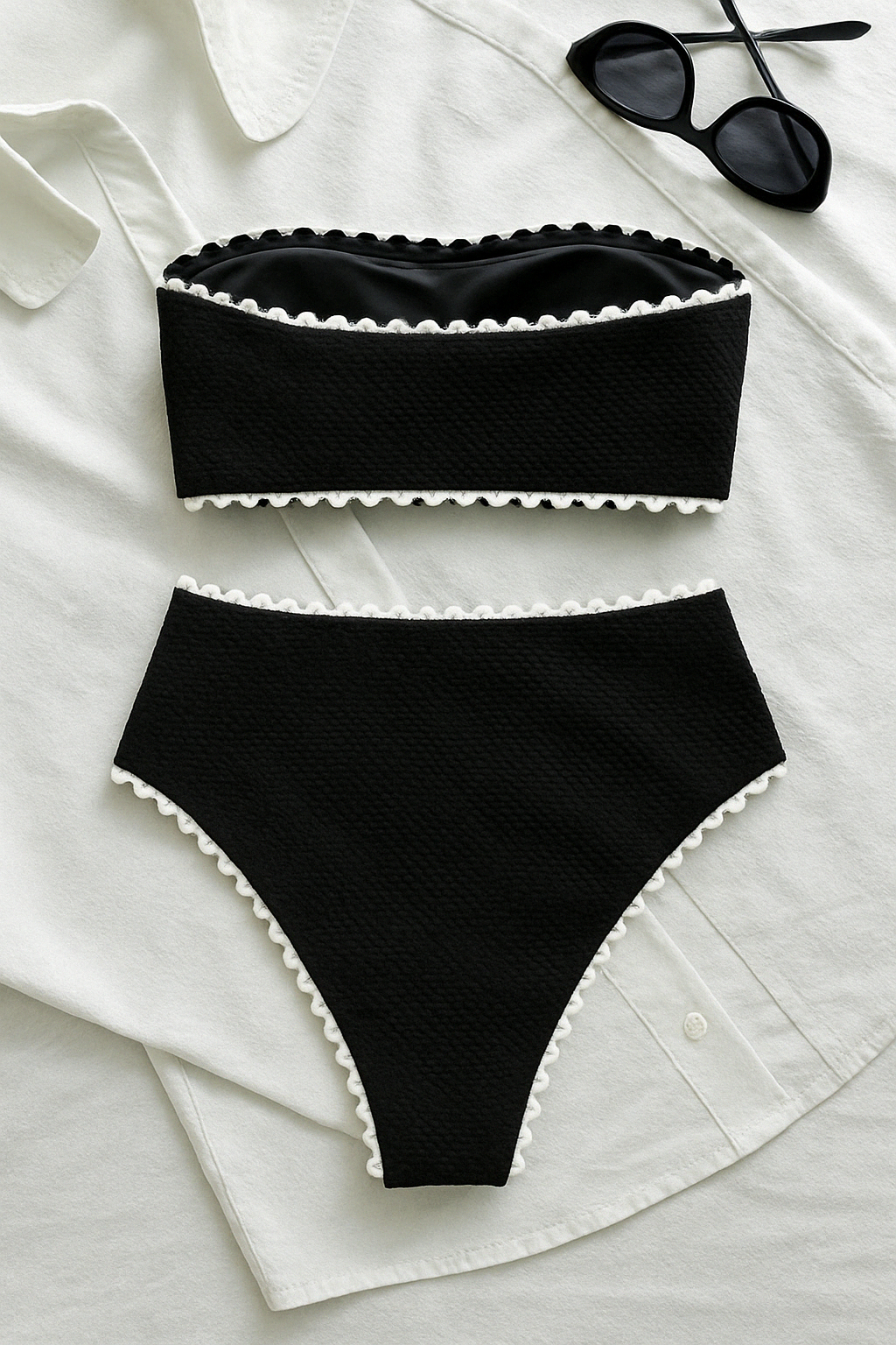 Black textured bandeau top and high-waist bikini bottom with white trim, laid flat on a white shirt