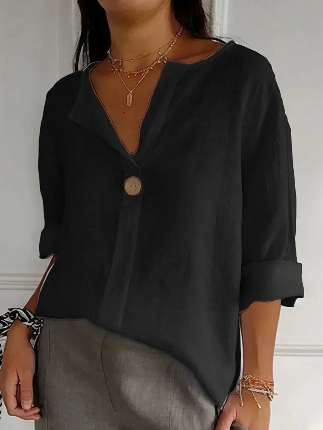 Woman wearing a black linen V-neck blouse with a single button and rolled sleeves