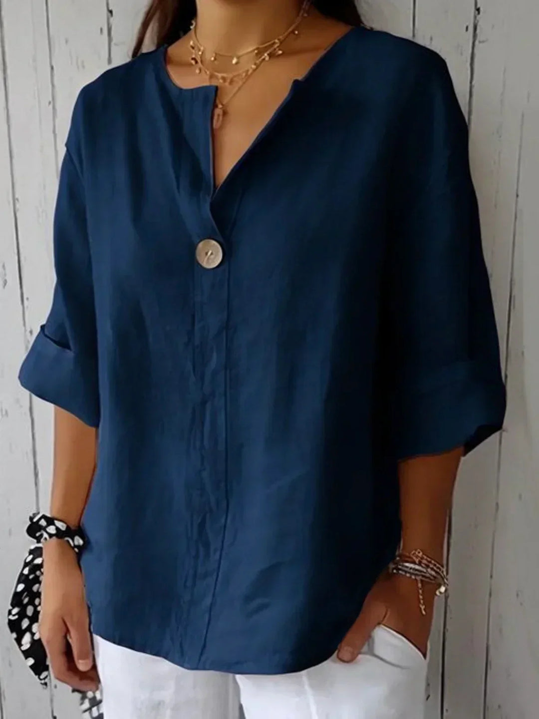 Woman wearing a navy blue linen V-neck blouse with a single button and rolled sleeves