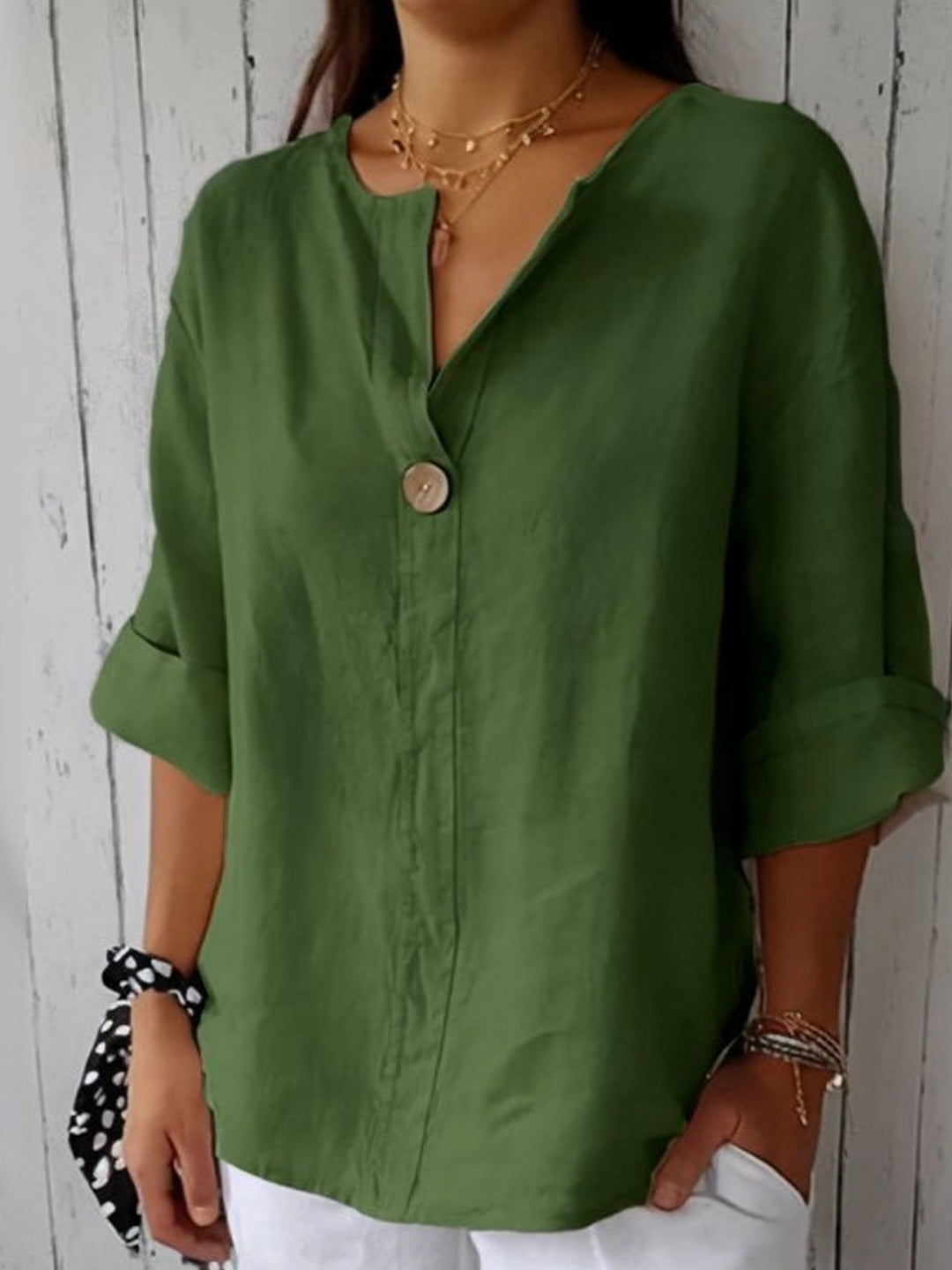 Woman wearing an olive green linen V-neck blouse with a single button and rolled sleeves