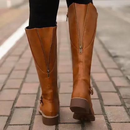 Back view of tan brown knee-high boots with a side zipper on a brick pavement