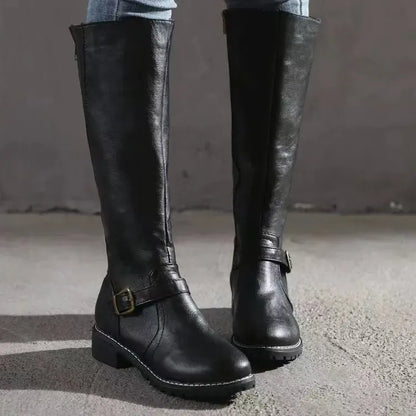 Black knee-high boots with a buckle strap and a low heel, worn with jeans