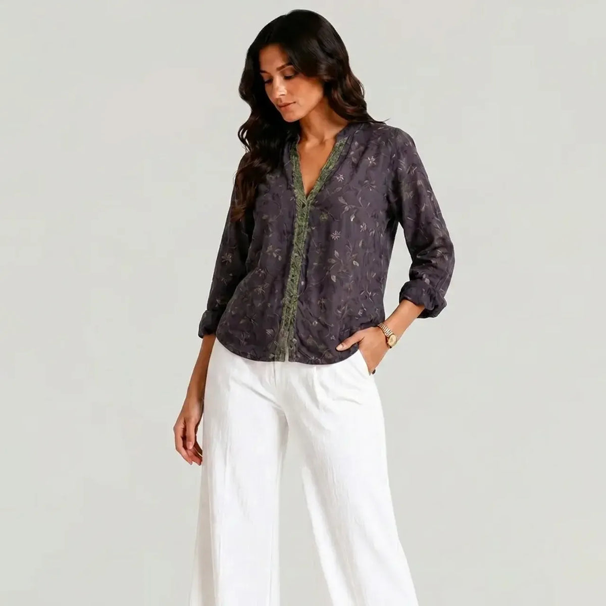 Full view of the dark purple boho V-neck blouse with green trim worn with white wide-leg pants