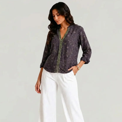 Full view of the dark purple boho V-neck blouse with green trim worn with white wide-leg pants
