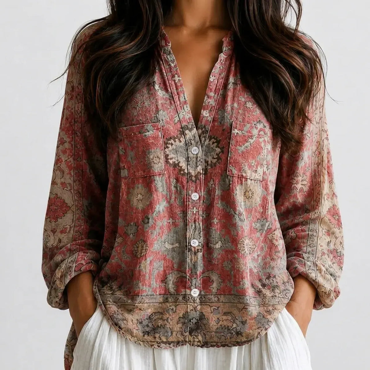 Woman wearing a pink and red paisley boho V-neck blouse with a brooch detail and white pants