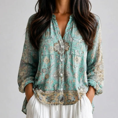 Woman wearing a teal and beige printed boho V-neck blouse with a brooch detail and white pants