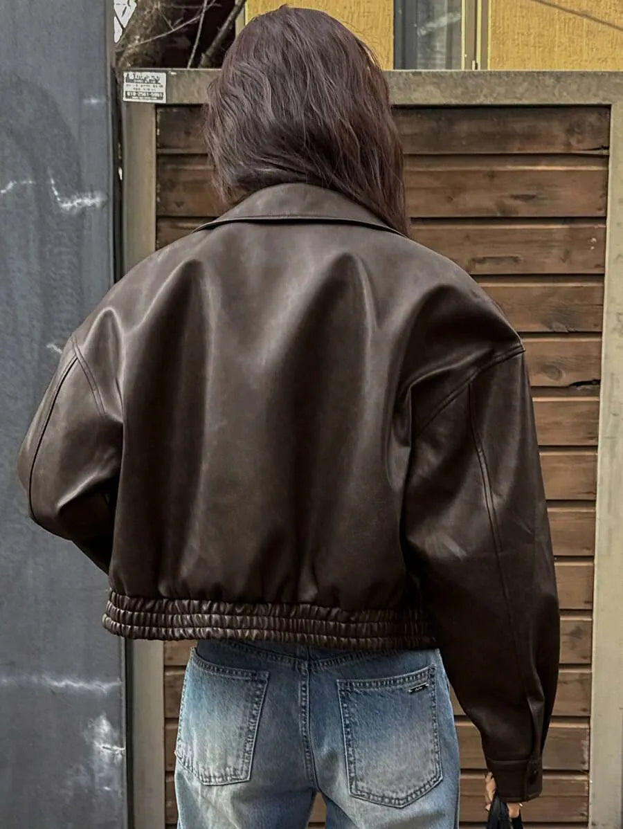 Back view of the cropped dark brown leather-look jacket with an elastic hem and light-wash jeans