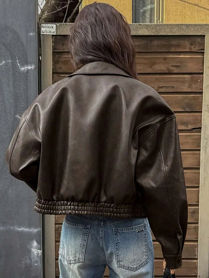Back view of the cropped dark brown leather-look jacket with an elastic hem and light-wash jeans