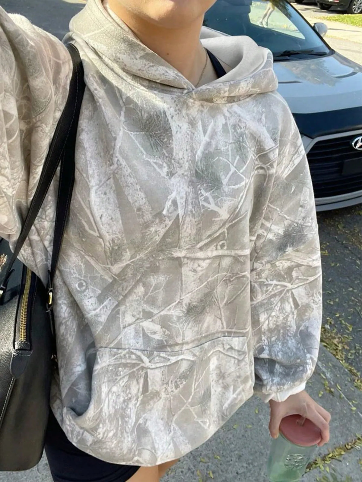 Woman wearing a light grey oversized hoodie with a crackled branch print and carrying a black bag