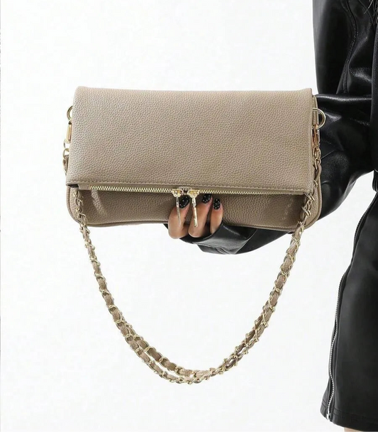 Taupe fold-over bag with a gold chain strap, held in front of a black leather jacket