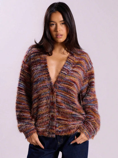 Woman wearing a multicolor rust and purple striped fuzzy knit cardigan with an open front and dark jeans