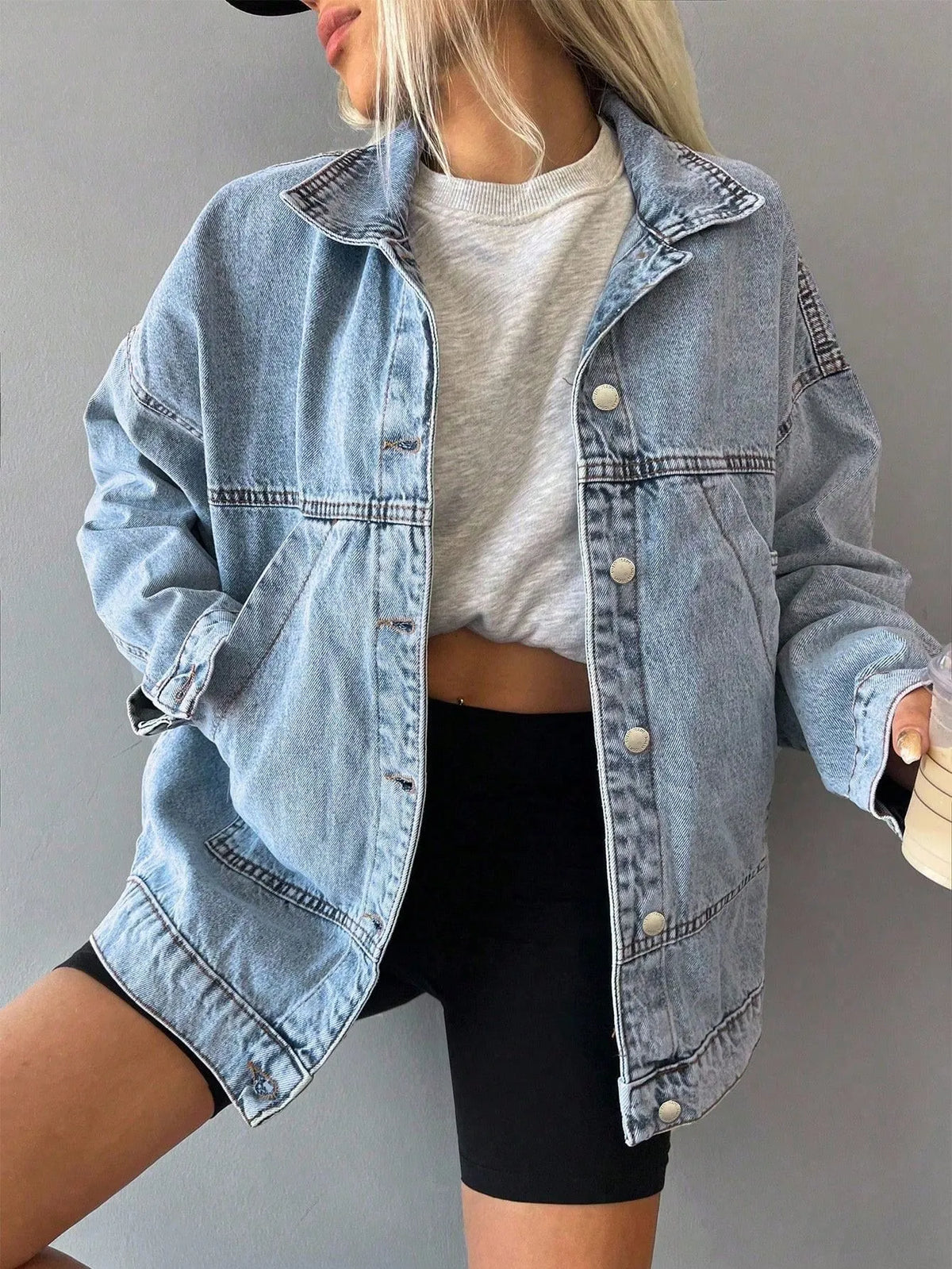 Woman wearing an oversized light-wash denim jacket over a white top and black bike shorts, front view