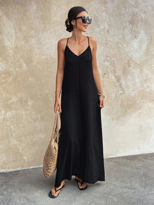 Woman wearing a black spaghetti-strap long dress with a woven straw bag, front view