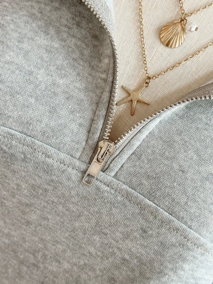 Close-up of the half zipper and collar of the light grey sweatshirt with layered necklaces