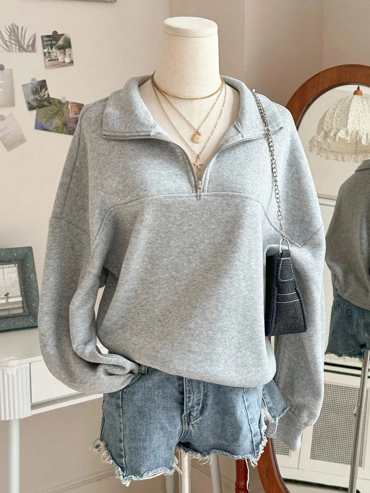 Light grey oversized quarter-zip sweatshirt with a folded collar, styled on a mannequin with denim shorts