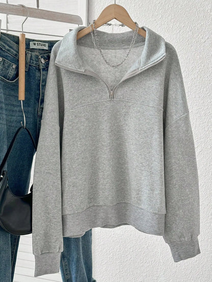 Light grey quarter-zip sweatshirt on a hanger next to blue jeans