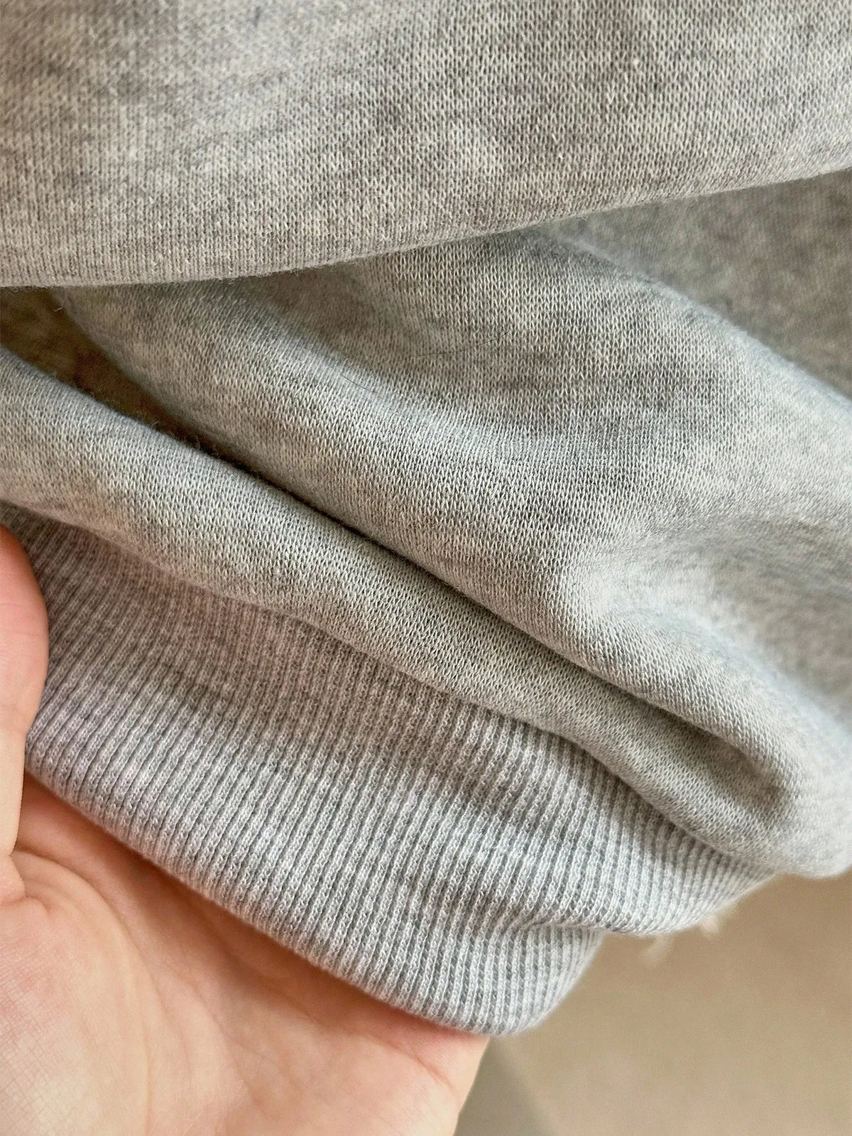 Close-up of the ribbed cuff of the light grey sweatshirt held in a hand