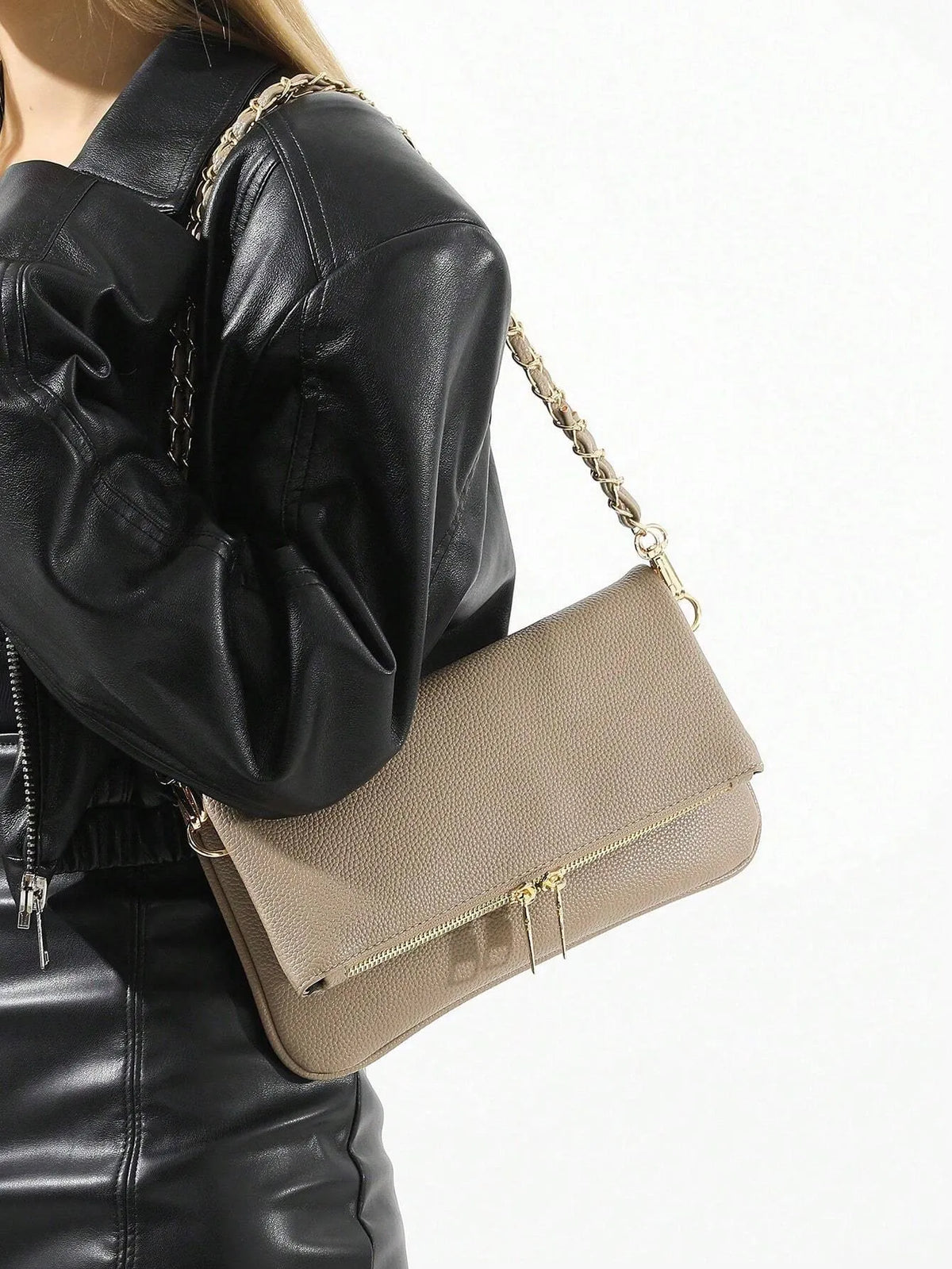 Taupe fold-over shoulder bag with a gold chain strap worn over a black leather jacket, side view