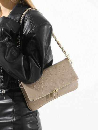Taupe fold-over shoulder bag with a gold chain strap worn over a black leather jacket, side view
