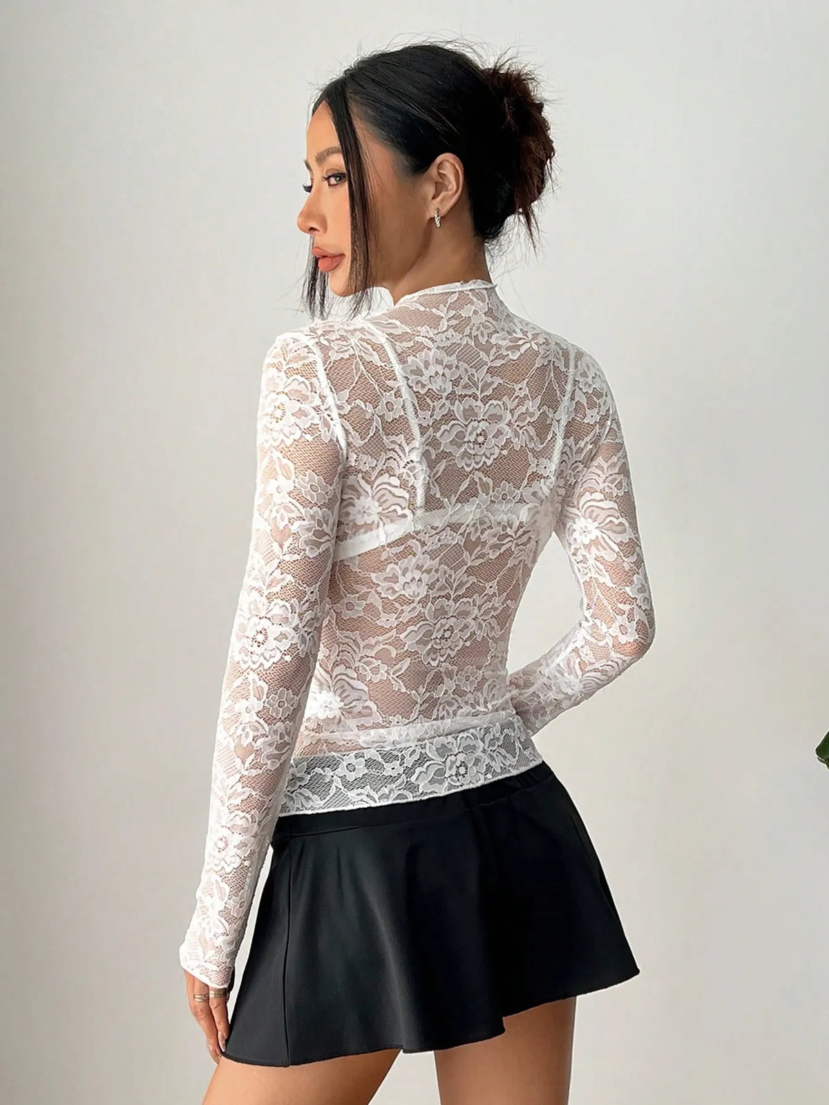 Three-quarter view of the white sheer lace long-sleeve top with a black flared skirt
