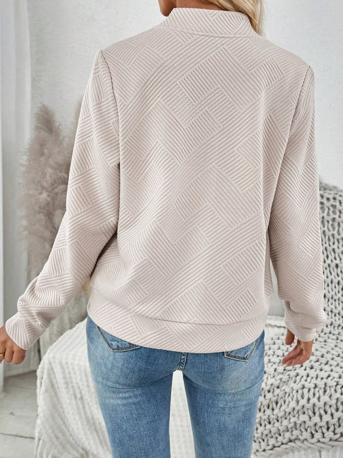 Back view of the beige textured bomber jacket with a ribbed hem and blue jeans