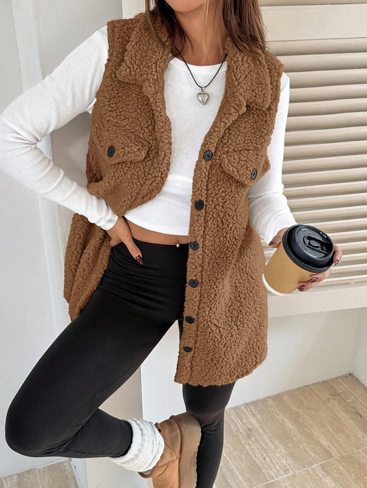 Woman wearing a brown teddy fleece button-front vest over a white long-sleeve top and black leggings, holding a coffee cup