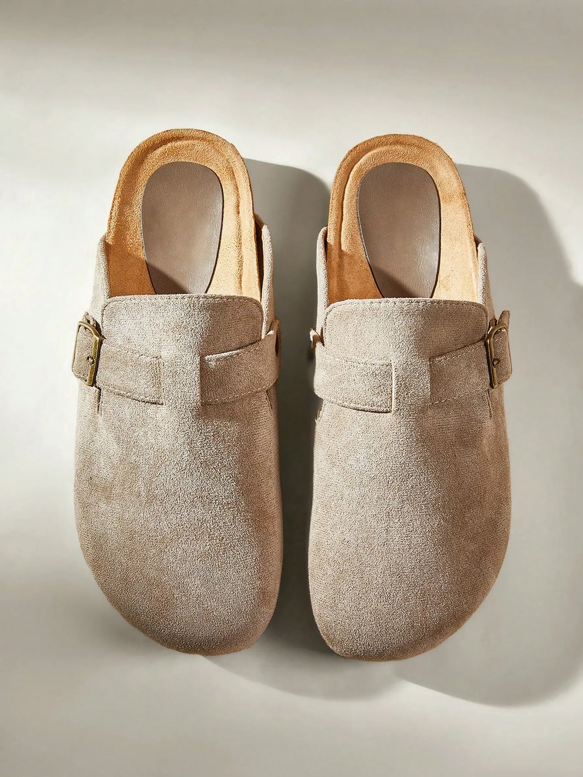 Pair of taupe suede clog-style slides with buckle straps, top view