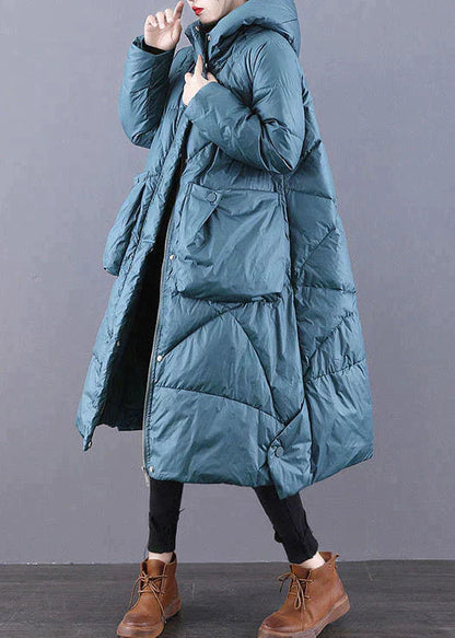 Woman wearing a long teal quilted hooded winter coat open at the front with black leggings and brown boots