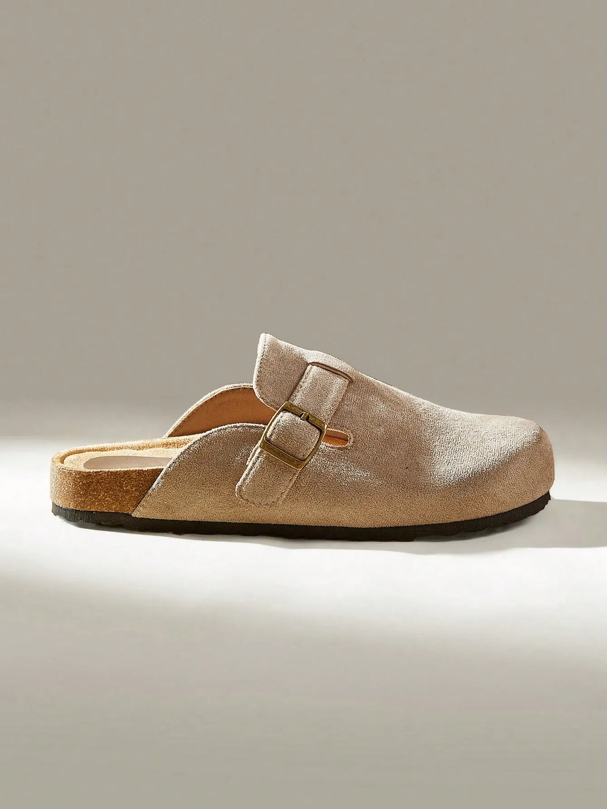 Side view of a taupe suede clog-style slide with a buckle strap and cork footbed