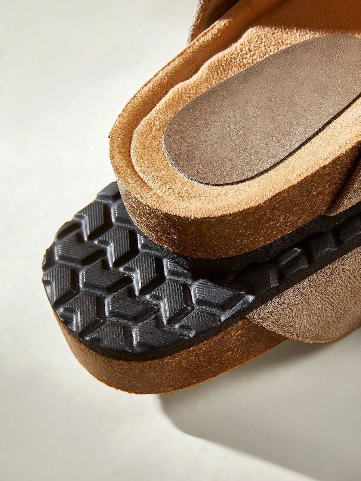 Close-up of the black textured sole and cork edge of a suede clog-style slide