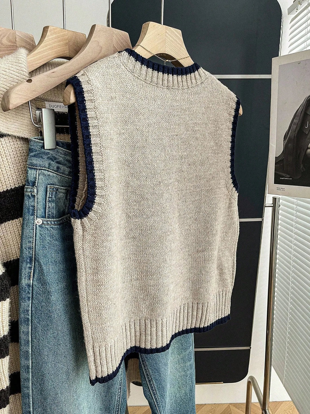 Grey knit sweater vest with navy contrast trim hanging on a hanger, front view